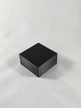 Load image into Gallery viewer, Black rectangular plastic enclosure or project box photographed on a white textured background. The box has a flat top surface with smooth sides and several small circular holes visible along the edges, suggesting mounting or assembly points. The object is positioned at a slight angle, showing the top and two side faces.