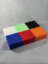 Load image into Gallery viewer, Six rectangular plastic blocks in white, green, black, blue, red, and orange are arranged in a compact 2-by-3 layout on a white textured fabric surface. The blocks are aligned to form a larger rectangular shape, with the white, green, and black blocks in the top row and the blue, red, and orange blocks in the bottom row. Small circular holes are visible on the front faces of several blocks, indicating mounting or assembly features. The photograph is taken from an elevated angle, showing the top surfaces and